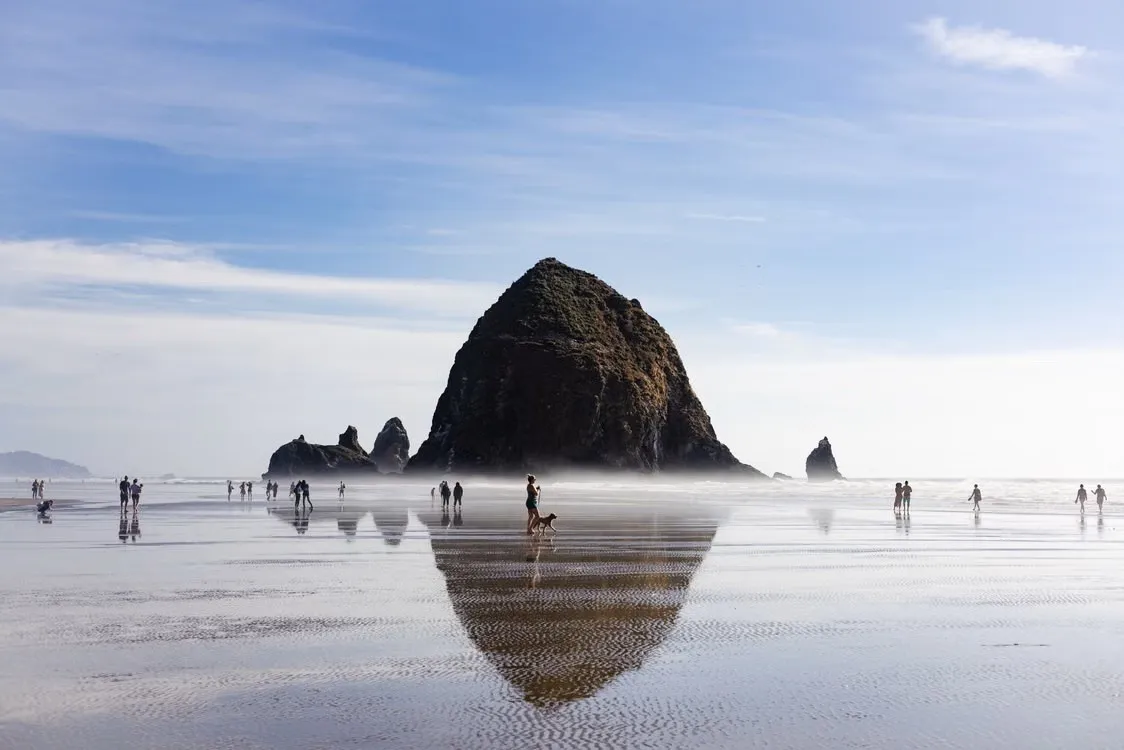 Haystack Rock at Cannon Beach at low tide, with families walking on the wet sand